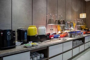 Una mesa de buffet con varios recipientes de comida, una máquina de café y un dispensador de agua.