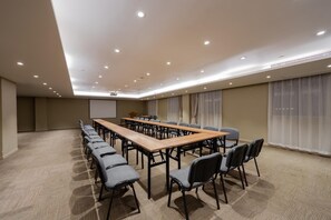 Una sala de conferències amb una taula llarga, cadires, una pantalla de projector i un paviment amb moqueta.