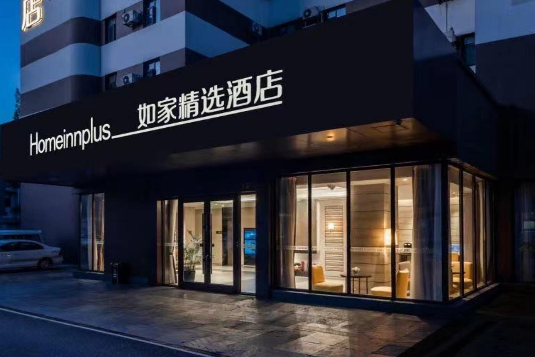 A hotel entrance with a sign reading 'Homeinnplus' and a glass facade.