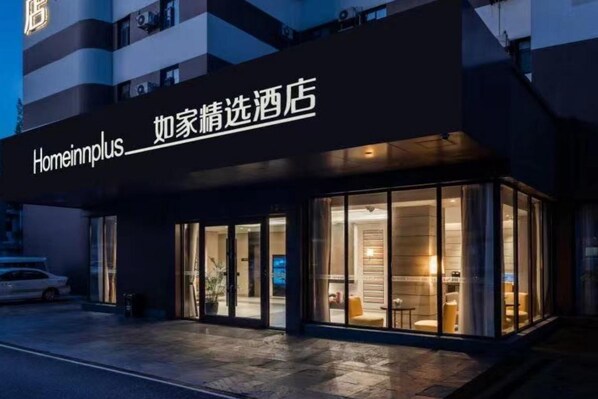 L’entrée d’un hôtel, avec une enseigne indiquant « Homeinnplus » et une façade en verre.