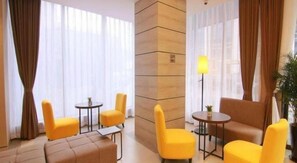 A hotel lobby with yellow chairs, a sofa, a small table, and a lamp.