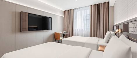 Een hotelkamer met twee bedden, een aan de muur bevestigde televisie, een klein tafeltje met een stoel, en een raam met gordijnen.