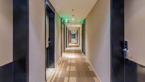 A hotel corridor with doors on both sides, a patterned carpet, and a green exit sign. - Homeinn Plus (beijing Zhongguancun Wudaokou (Beijing)