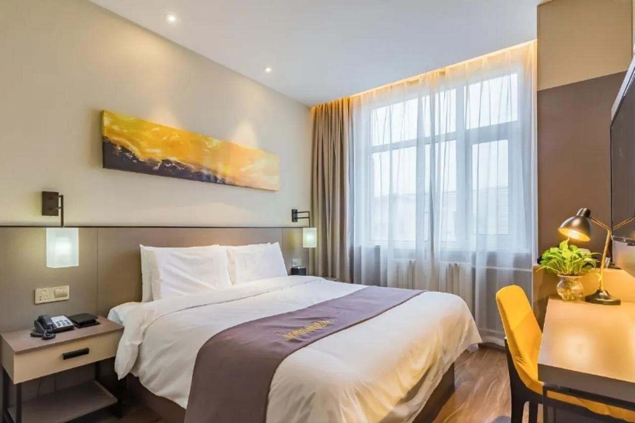 Habitación de hotel con una cama grande, mesitas de noche, un escritorio con silla, un cuadro en la pared y una ventana con cortinas.