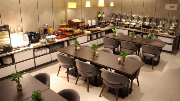 A modern dining area with multiple tables and chairs, a buffet counter with various food items, and hanging pendant lights. - Homeinn Plus (beijing Zhongguancun Wudaokou (Beijing)