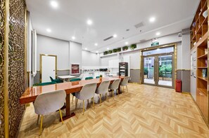 A modern dining area with a long wooden table, several chairs, and a kitchen in the background. - Homeinn Plus (beijing Zhongguancun Wudaokou (Beijing)