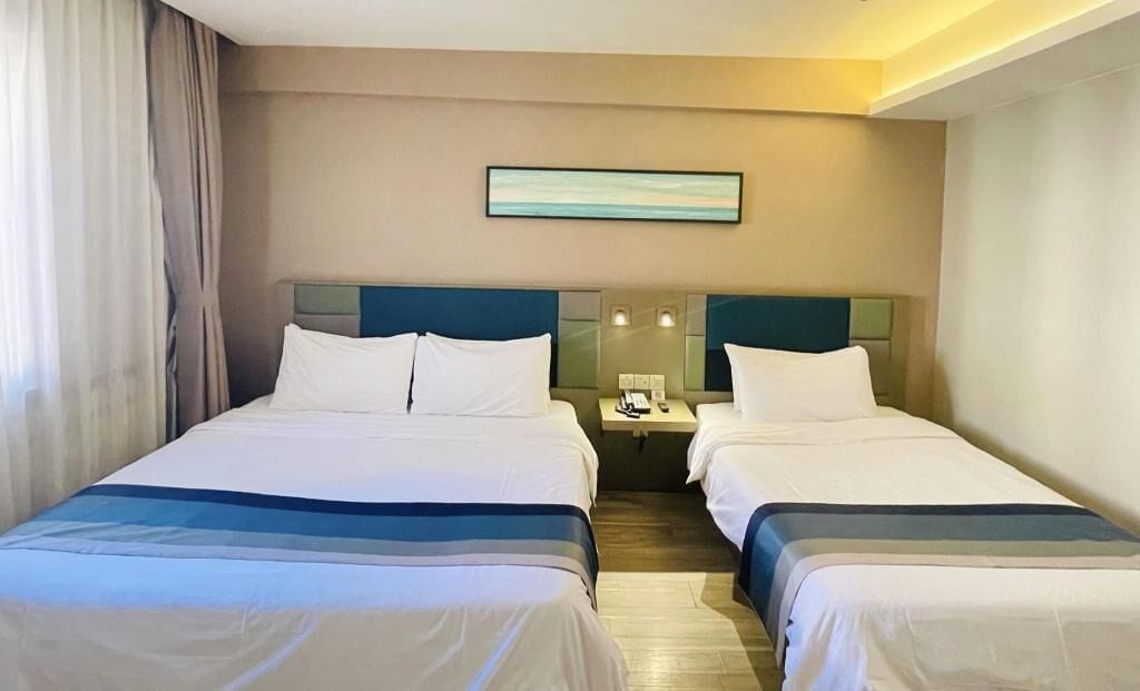 A hotel room with two beds, a nightstand, and a painting on the wall.