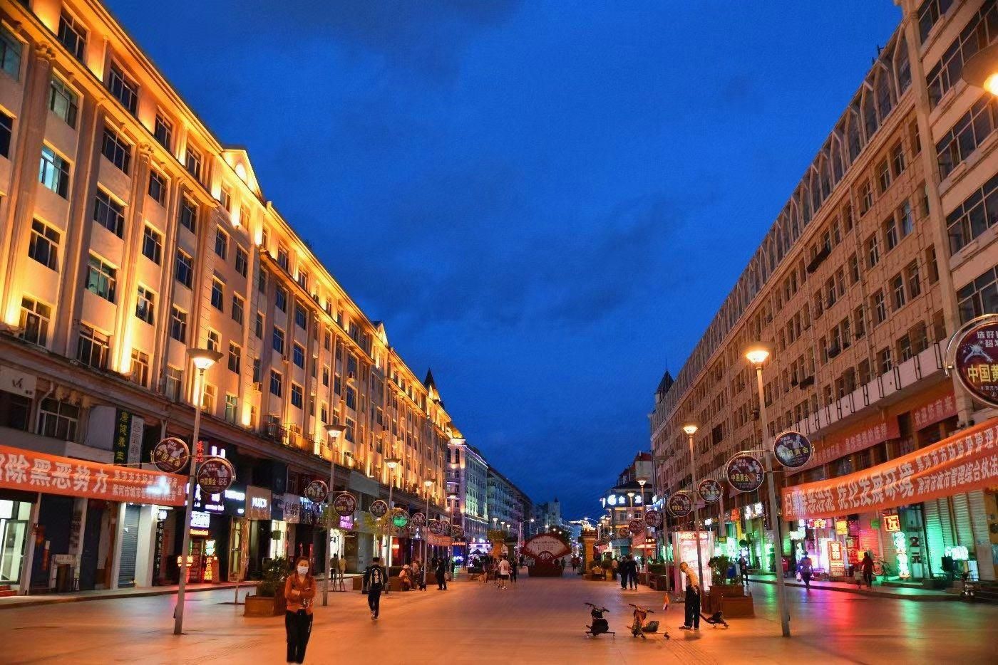 Une large rue bordée de bâtiments des deux côtés, éclairée par des lampadaires.