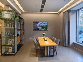 Un comedor moderno con una mesa de madera, sillas grises, un televisor montado en la pared y una estantería con diversos objetos.