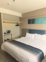 A hotel room with a large bed, a bedside table, a wall-mounted shelf, and a painting.