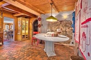 Ein rustikales Interieur mit Holzbalkendecke, Steinwand, rundem Tisch mit weißem Tuch und einer Pendelleuchte.