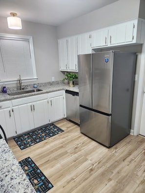 A kitchen with white cabinets, a stainless steel refrigerator, a granite countertop, a sink, and a window with blinds. - Spacious 4-bedroom house in pleasant Columbia with AC (Columbia)