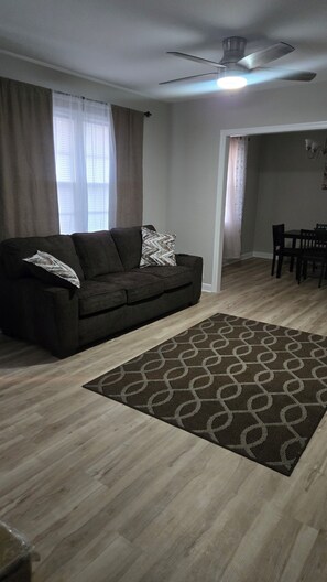 A living room with a dark sofa, a patterned rug, and a ceiling fan. - Spacious 4-bedroom house in pleasant Columbia with AC (Columbia)