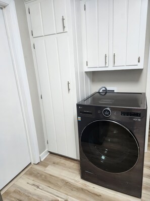 A compact laundry room with a front-loading washer and dryer, white cabinets, and a wooden floor. - Spacious 4-bedroom house in pleasant Columbia with AC (Columbia)