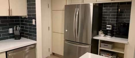 A modern kitchen with stainless steel appliances, white cabinetry, and a black tiled backsplash.
