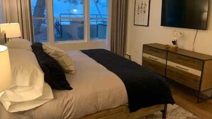 A bedroom with a bed, a TV, a dresser, and a window with a view of a snowy landscape. - Park City Condo – Pool, Hot Tub & Waffles (Park City)