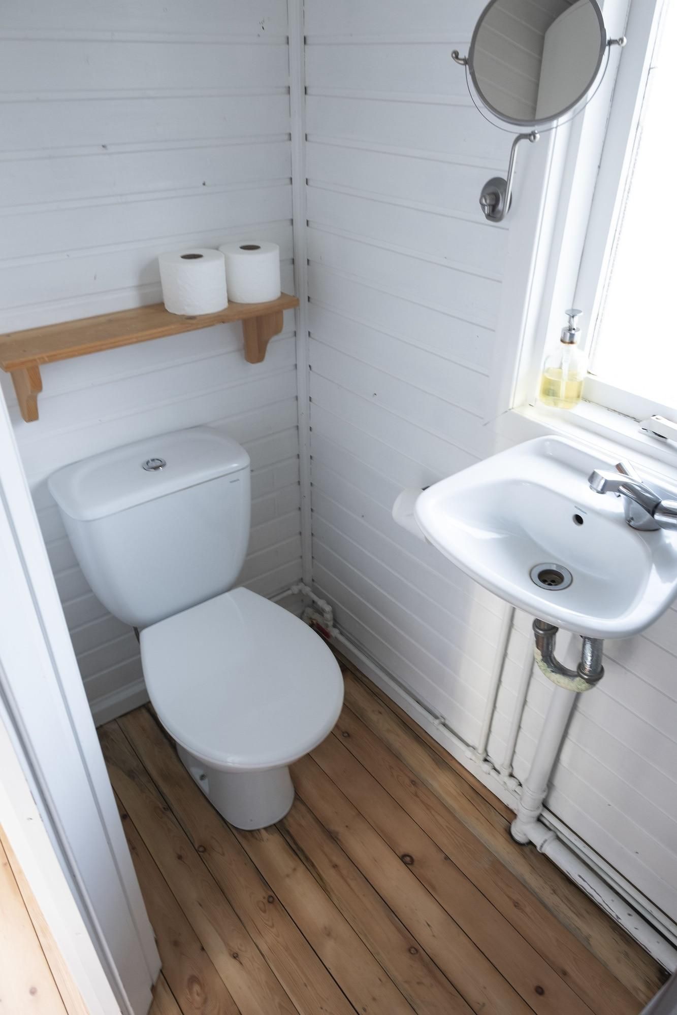 A small bathroom with a toilet, a sink, and a mirror. There are two rolls of toilet paper on a shelf.