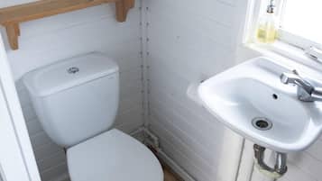 A small bathroom with a toilet, a sink, and a mirror. There are two rolls of toilet paper on a shelf.