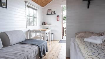 A cozy cabin interior with a sofa, a bed, a small table, and a window.