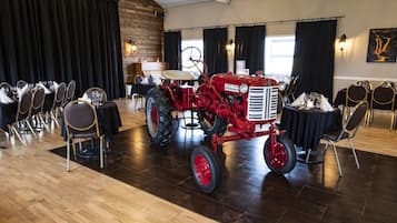 A dining area with tables set for a meal, a red tractor in the center, and a wooden wall with a window.