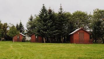 A row of red wooden cabins in a grassy field with dense trees in the background.