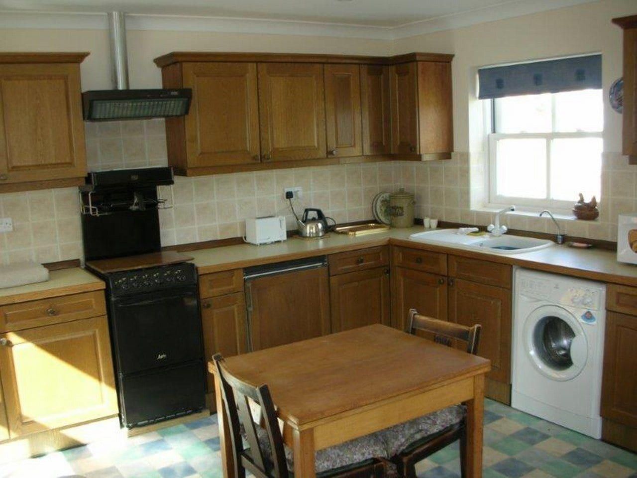 A compact kitchen with wooden cabinets, a black stove, a washing machine, and a dining table.