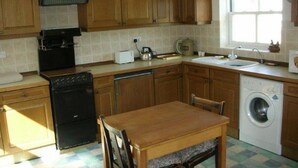A compact kitchen with wooden cabinets, a black stove, a washing machine, and a dining table. - Watermill Farm (Lincoln)