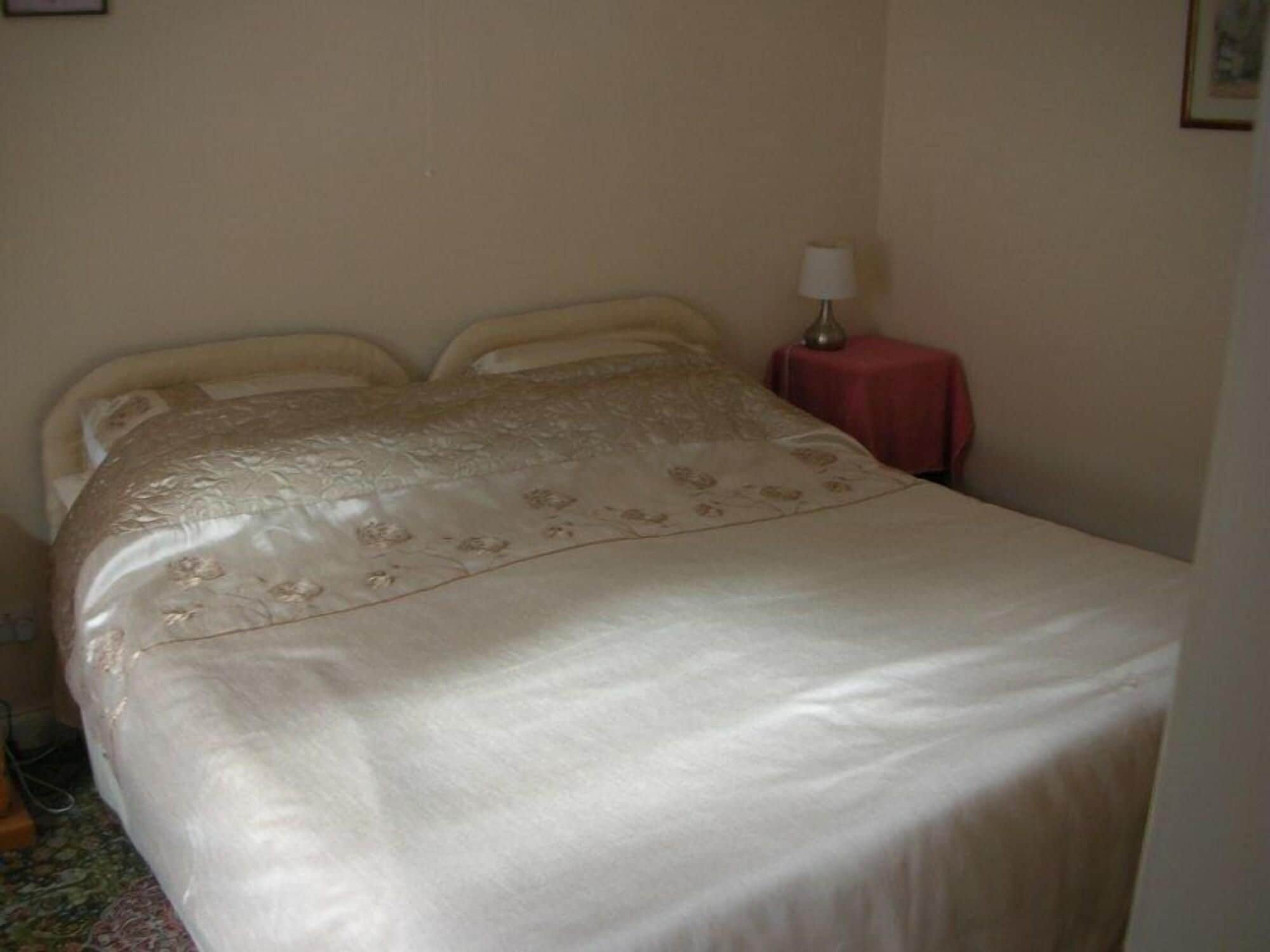 A bed with a floral-patterned bedspread, a bedside table with a lamp, and a small red tablecloth.