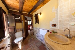 Une salle de bain avec un plafond en bois, des toilettes blanches, un lavabo avec un plan de toilette en bois et un mur recouvert de carreaux.