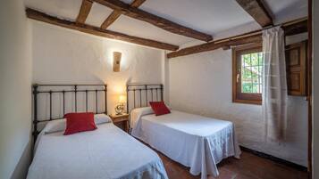 A room with two single beds, a window with curtains, and a wooden ceiling.