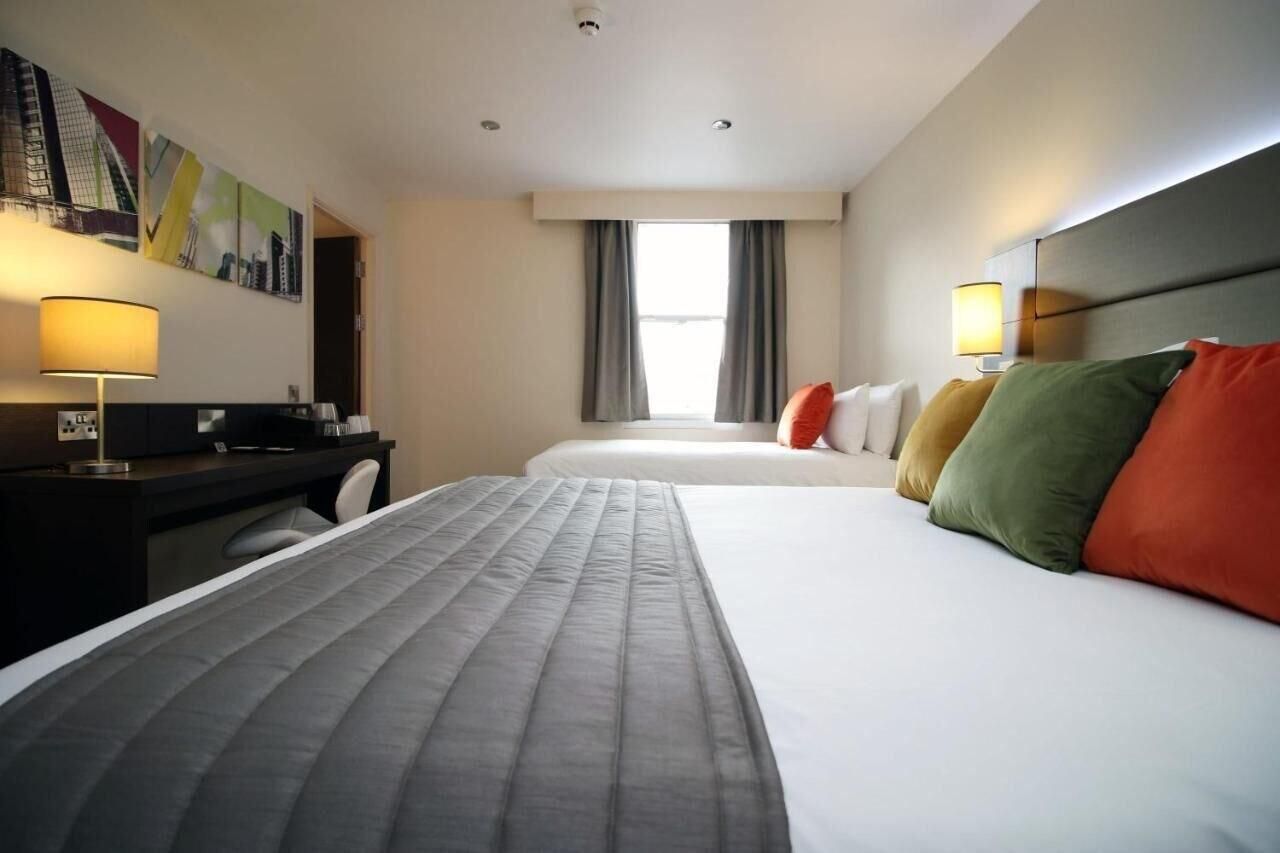 Habitación de hotel con dos camas, un escritorio y una ventana con cortinas.