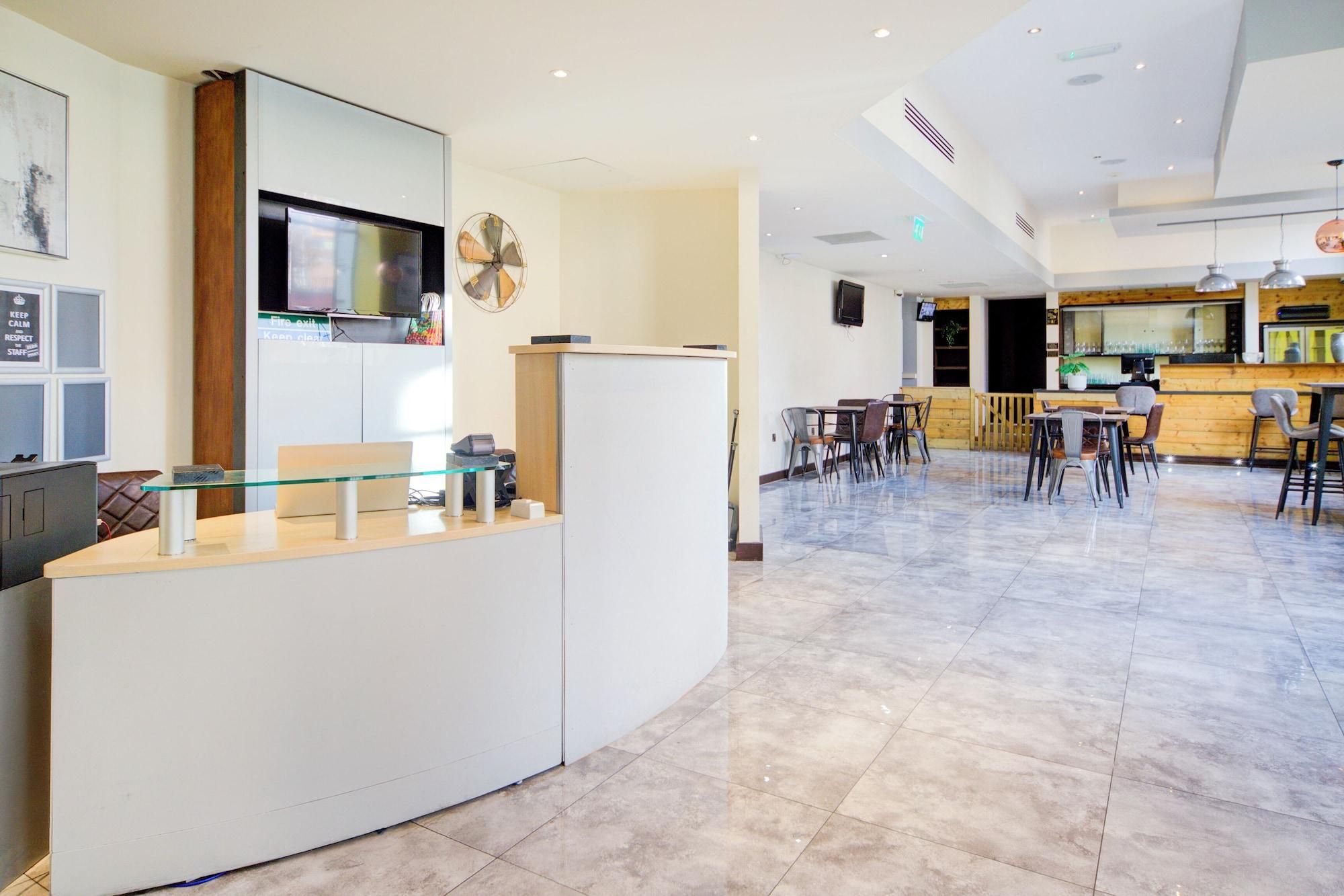 A modern hotel lobby with a reception desk, seating area, and a bar.