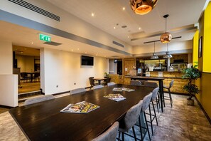 Un hall d’hôtel moderne avec une longue table à manger, des sièges confortables, un bar et un panneau indiquant la sortie.