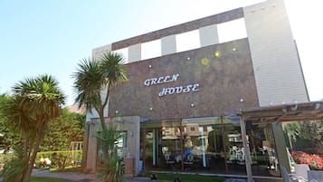 Un edificio con un cartel que dice 'GREEN HOUSE' y un área de estar al aire libre cubierta, con mesas y sillas.