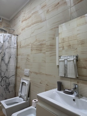 A bathroom with a shower curtain, a toilet, a sink, and a towel rack. - Hotel Green House (Berat)