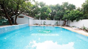 A swimming pool with a tiled edge, surrounded by a white wall and trees.