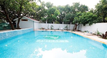 Una piscina con borde de azulejos, rodeada por un muro blanco y árboles.