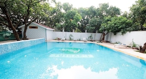 A swimming pool with a tiled edge, surrounded by a white wall and trees.