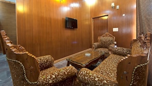 A room with wooden panel walls, a flat-screen TV mounted on the wall, and ornate upholstered furniture. - Tuskar S By Khurafati Nitin (Ramnagar)