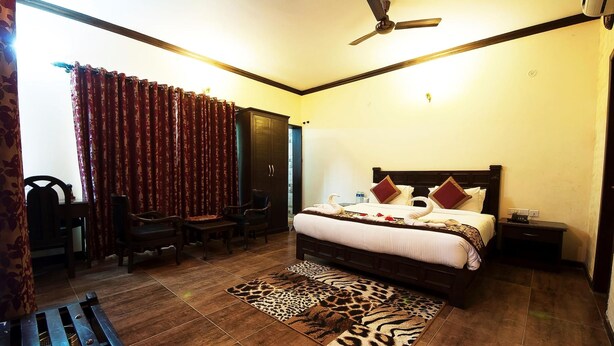 A hotel room with a bed, a desk, a chair, a sofa, a ceiling fan, and a patterned rug.