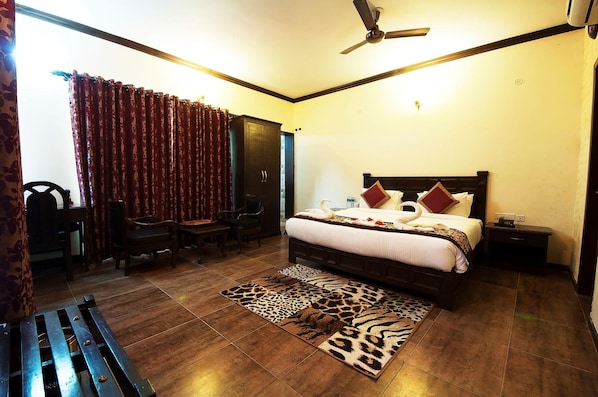 A hotel room with a bed, a desk, a chair, a sofa, a ceiling fan, and a patterned rug.