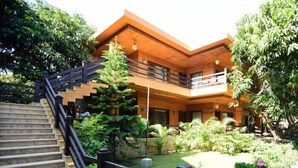 A two-story building with a wooden exterior, a staircase with a black railing, and a garden with various plants and flowers.