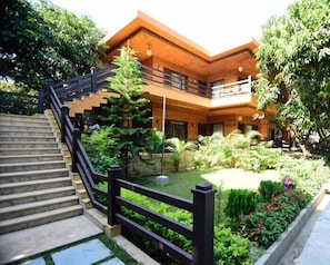 A two-story building with a wooden exterior, a staircase with a black railing, and a garden with various plants and flowers.