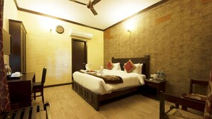 A hotel room with a bed, a chair, a desk, a wall clock, and a ceiling fan. - Tuskar S By Khurafati Nitin (Ramnagar)