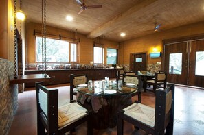 Un comedor con una mesa redonda de cristal, sillas de madera y una pared de piedra.