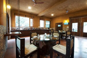 Un comedor con una mesa redonda de cristal, sillas de madera y una pared de piedra.