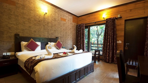 A hotel room with a large bed, a wooden headboard, a desk, and a window with curtains. - Tuskar S By Khurafati Nitin (Ramnagar)