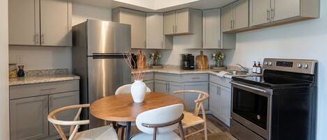 Una cocina moderna con armarios grises, un refrigerador de acero inoxidable, un horno negro y una mesa de comedor de madera con sillas.