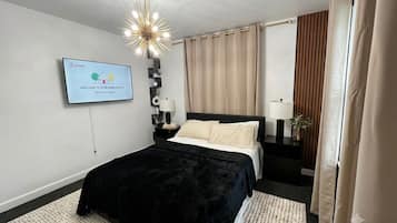 Ein modernes Hotelzimmer mit einem Bett, einem an der Wand befestigten Fernseher, einer Kristallleuchtreiter und Vorhängen.