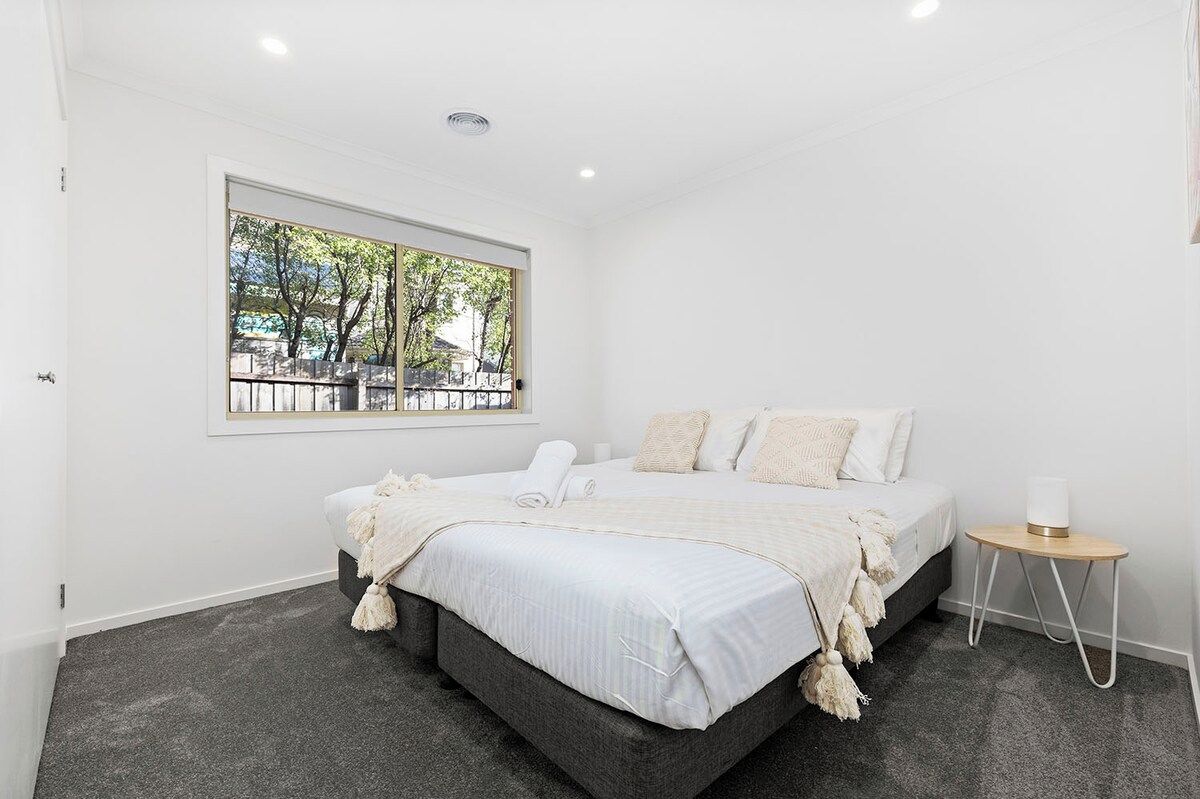 A bedroom with a large bed, a window with a view, and a bedside table with a lamp.